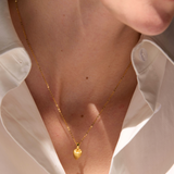 Gold necklace with a heart pendant worn by a person in a white shirt, branded 'Celestes Jewelry'.