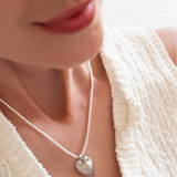 Close-up of a person wearing a pearl necklace with a heart pendant, brand 'Celestes' visible.