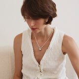 A woman wears a pearl necklace with heart pendant using a laptop on a white couch.