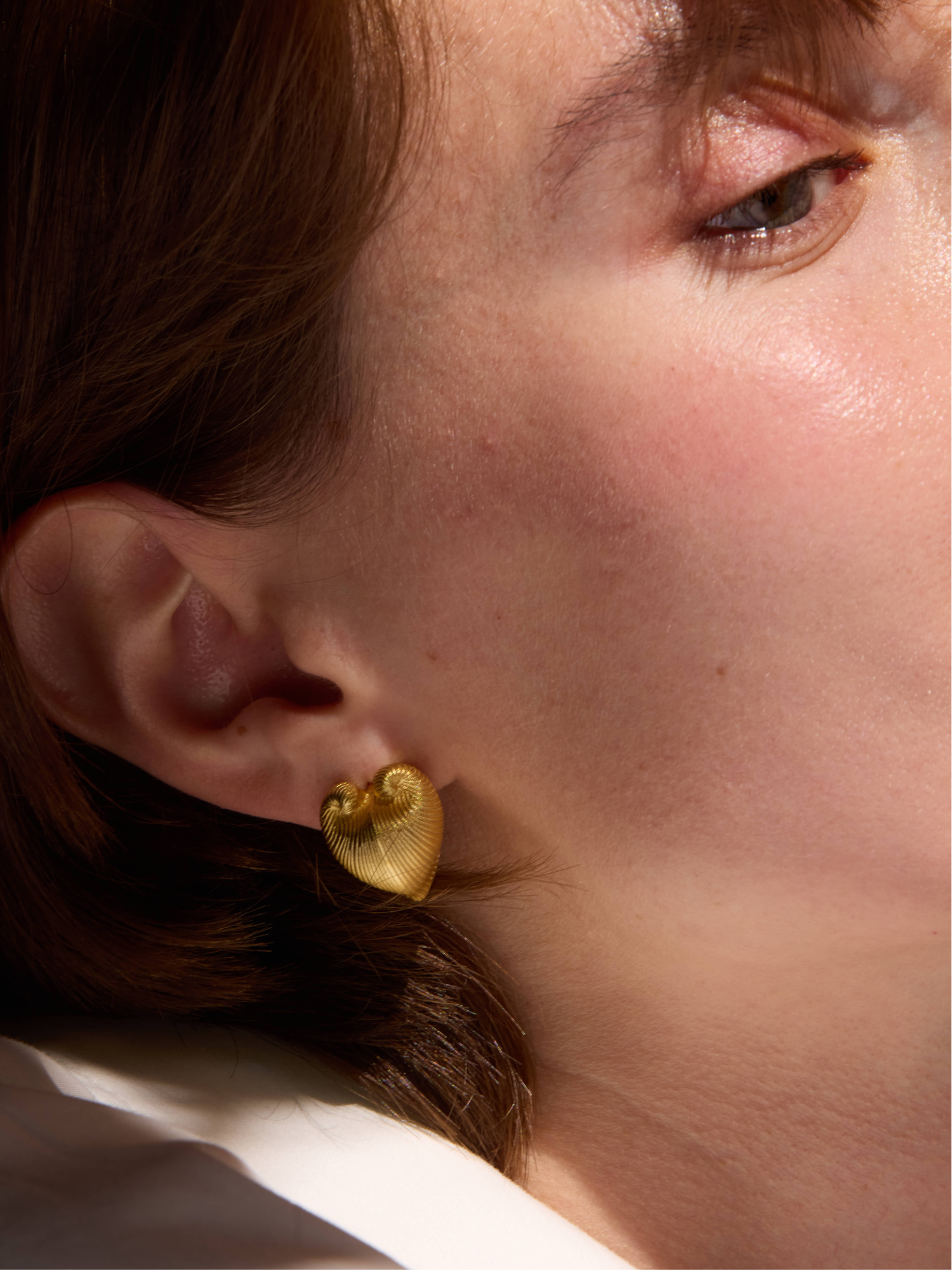 Close-up of a person wearing gold heart-shaped earrings.