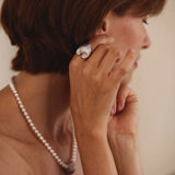 Woman adjusting an earring with a pearl necklace