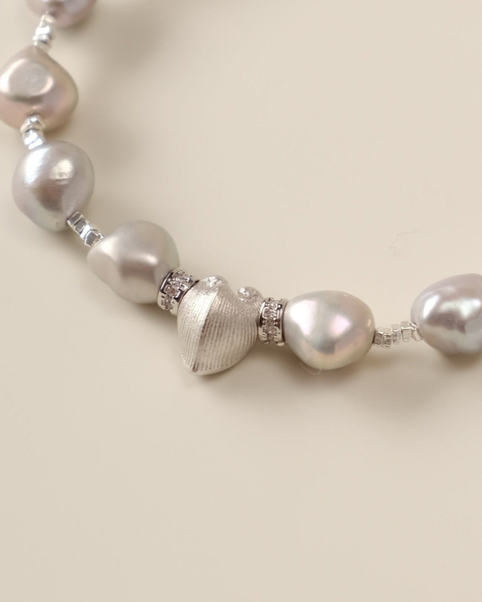 A celestial dance of contrasts, the Meiocardia Vulgaris & Keshi Pearl Bracelet unites the raw magic of ocean-born treasures with the shimmering mystery of the cosmos. Designed for free spirits who embrace imperfection as art, this piece blends a rare heart-shaped shell bead with the organic allure of keshi pearls—a testament to beauty forged in nature’s unpredictable hands.
Design & Craftsmanship:
- Dual-Perspective Heart Charm: The focal 8.0*9.8mm Meiocardia vulgaris bead, cast in hypoallergenic S925 silve