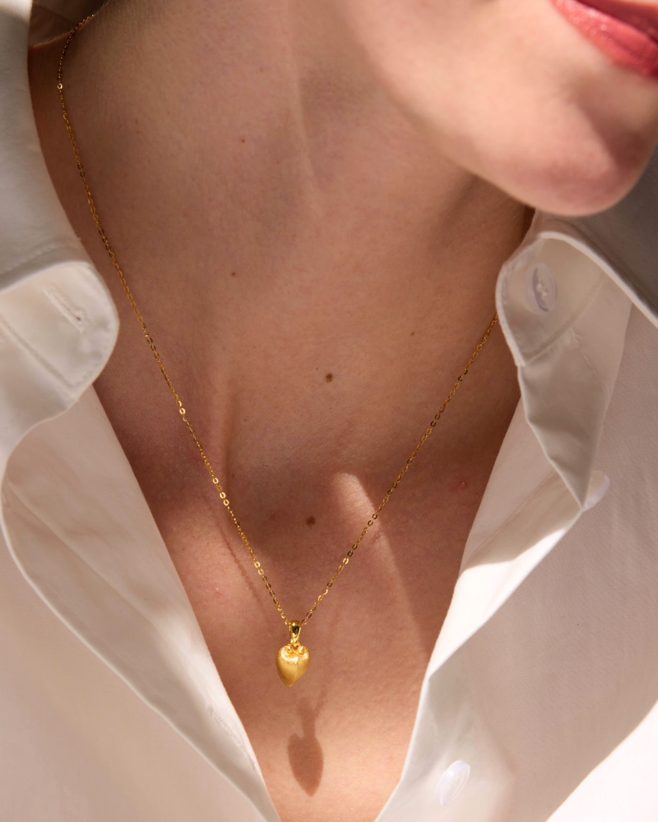 Gold necklace with a heart pendant worn by a person in a white shirt, branded 'Celestes Jewelry'.