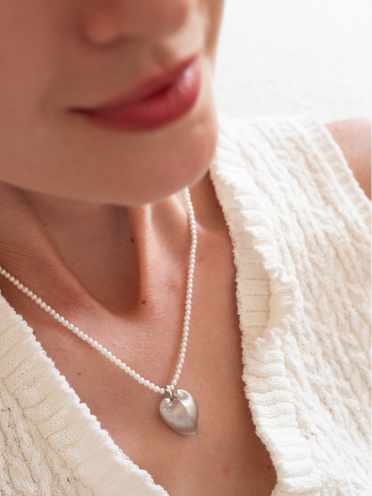 Close-up of a person wearing a pearl necklace with a heart pendant, brand 'Celestes' visible.