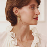 Woman wearing a white blouse with ruffled details and gold jewelry.