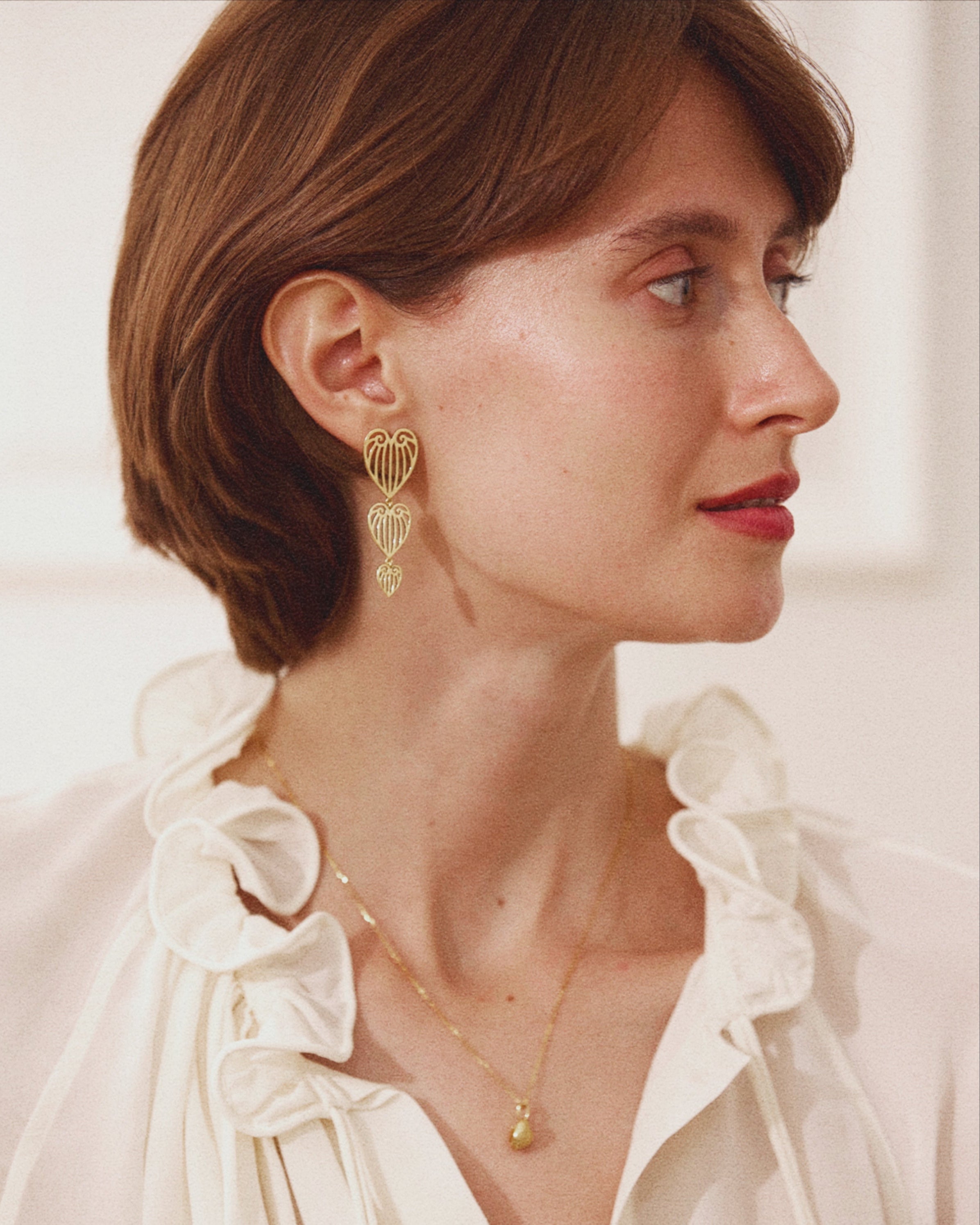 Woman wearing a white blouse with ruffled details and gold jewelry.