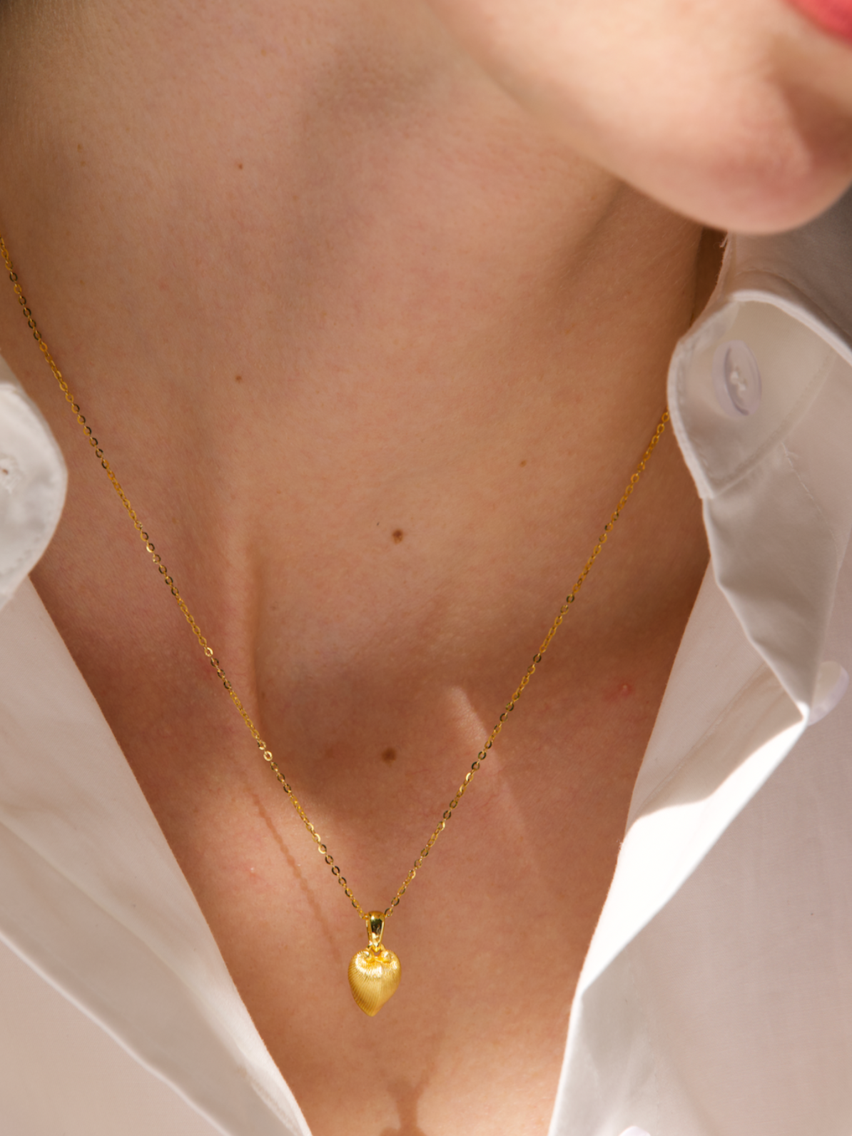 Gold necklace worn by a person with a white shirt, brand 'Celestes' visible.