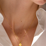 Gold necklace worn by a person with a white shirt, brand 'Celestes' visible.