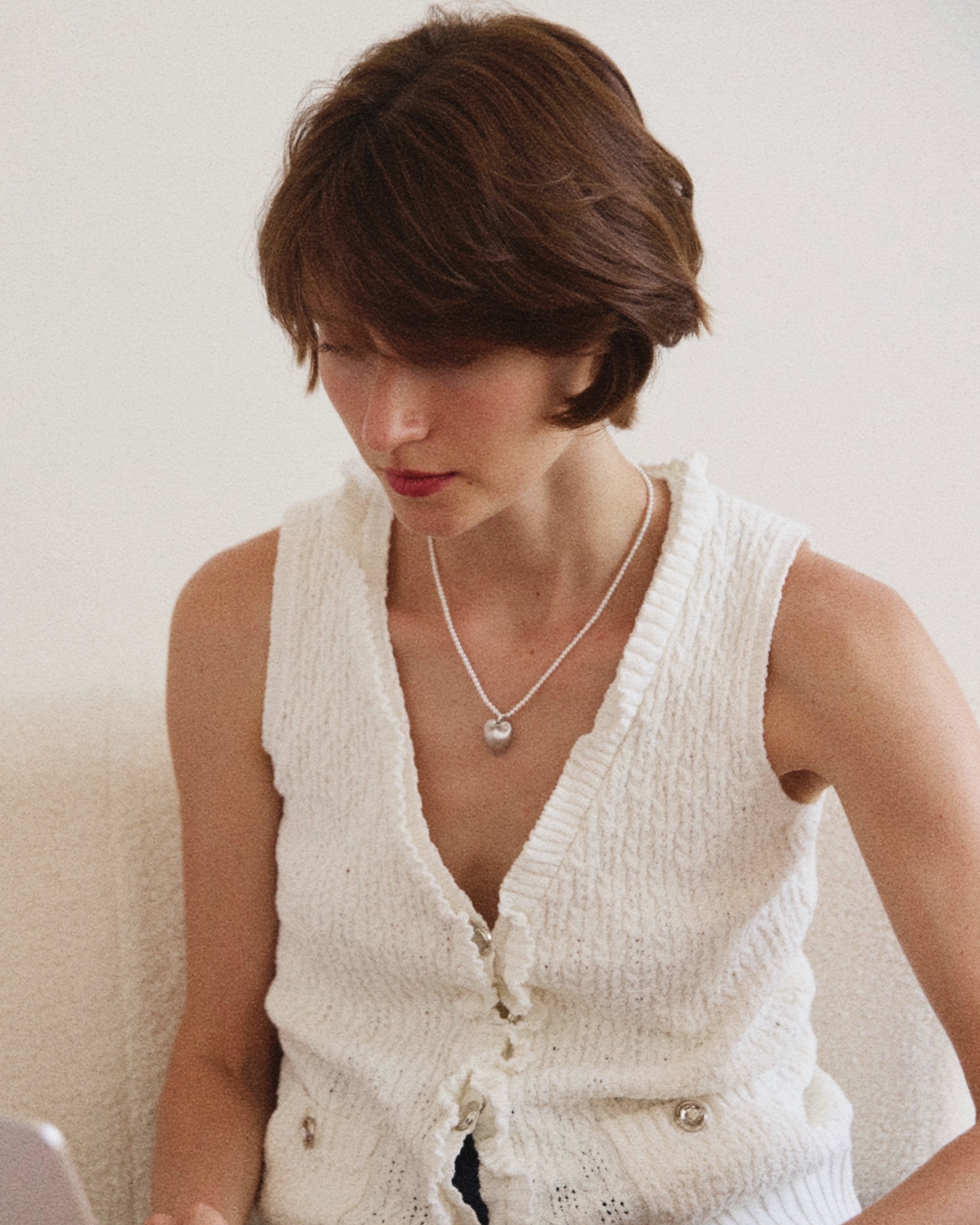 A woman wears a pearl necklace with heart pendant using a laptop on a white couch. 