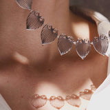 Close-up of a silver necklace with leaf-shaped pendants on a person wearing a white top.