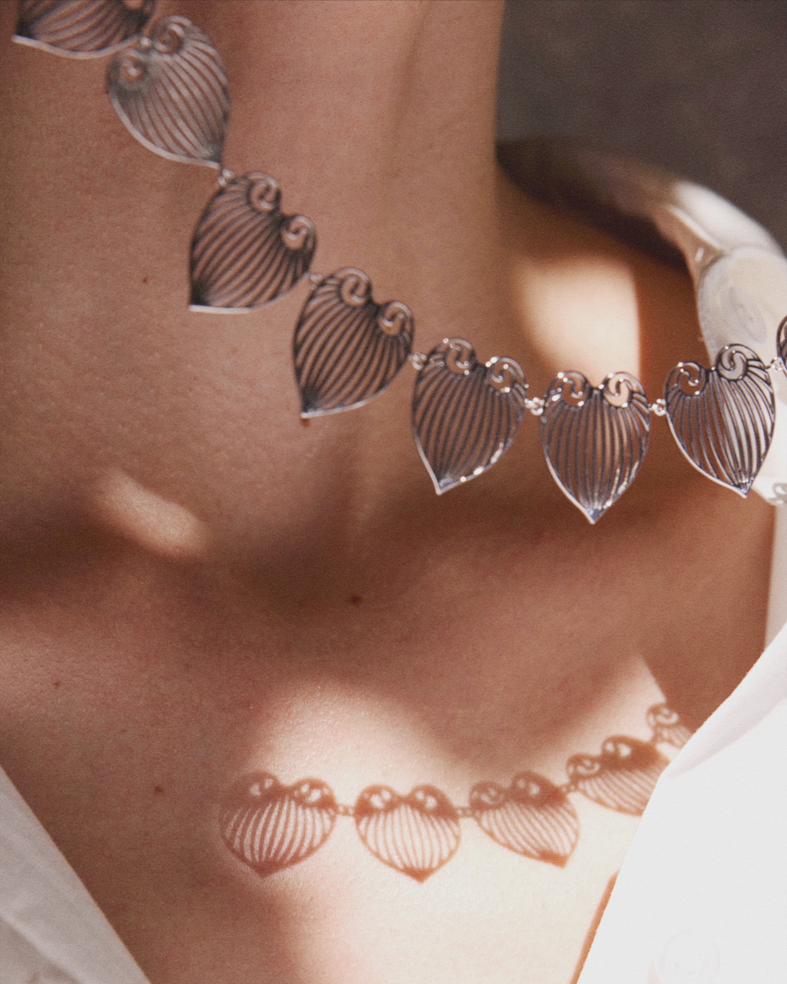 Close-up of a silver necklace with leaf-shaped pendants on a person wearing a white top.