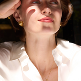 Woman shielding her eyes from the sun with a hand, wearing gold jewelry, with 'Celestes' branding.