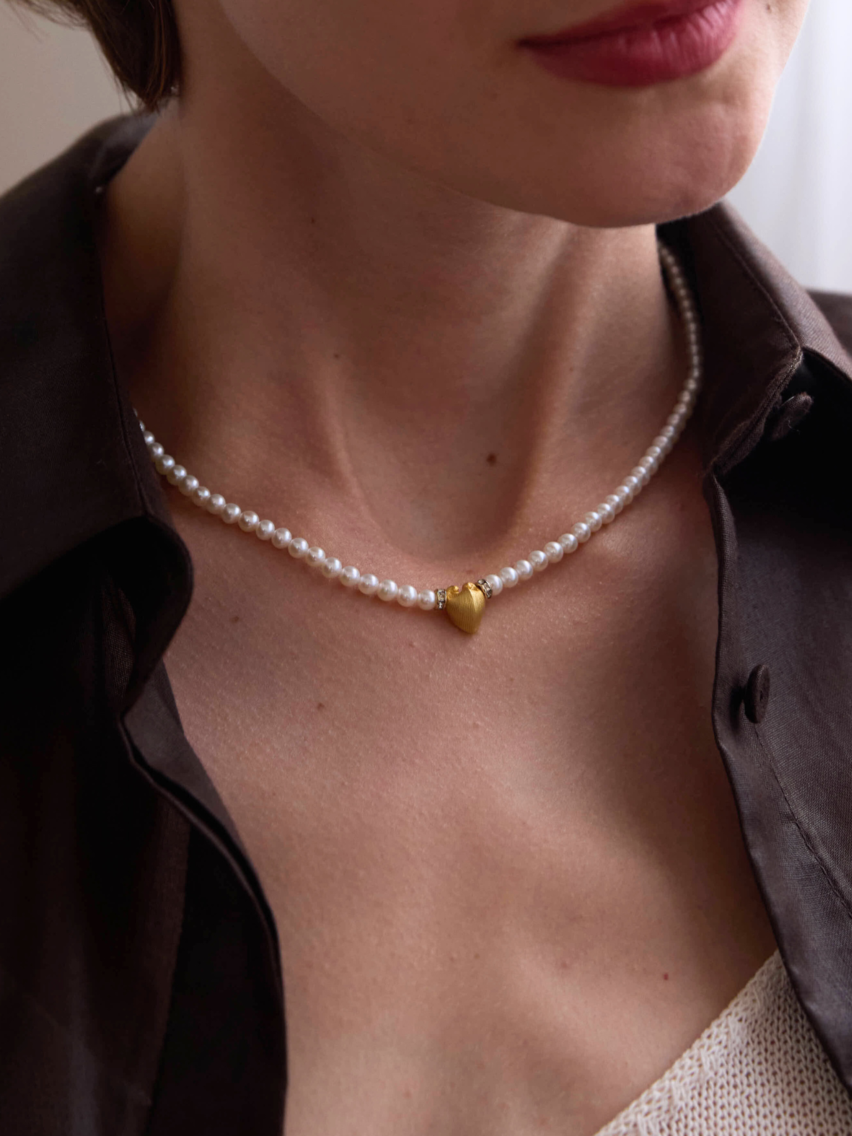 Pearl necklace with a gold heart pendant worn by a person, with 'Celestes Jewelry' branding.