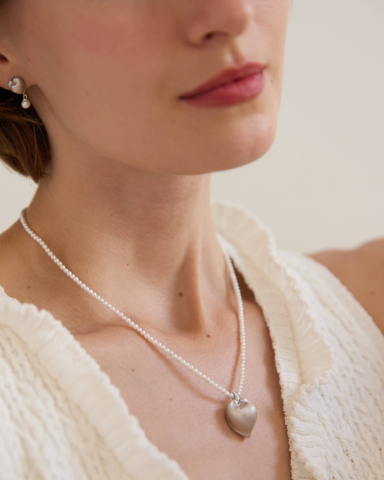 Close-up of a person wearing a pearl necklace with a heart pendant, with 'Celestes' branding.