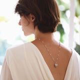 Woman wearing a white open-back dress with a necklace, standing outdoors.