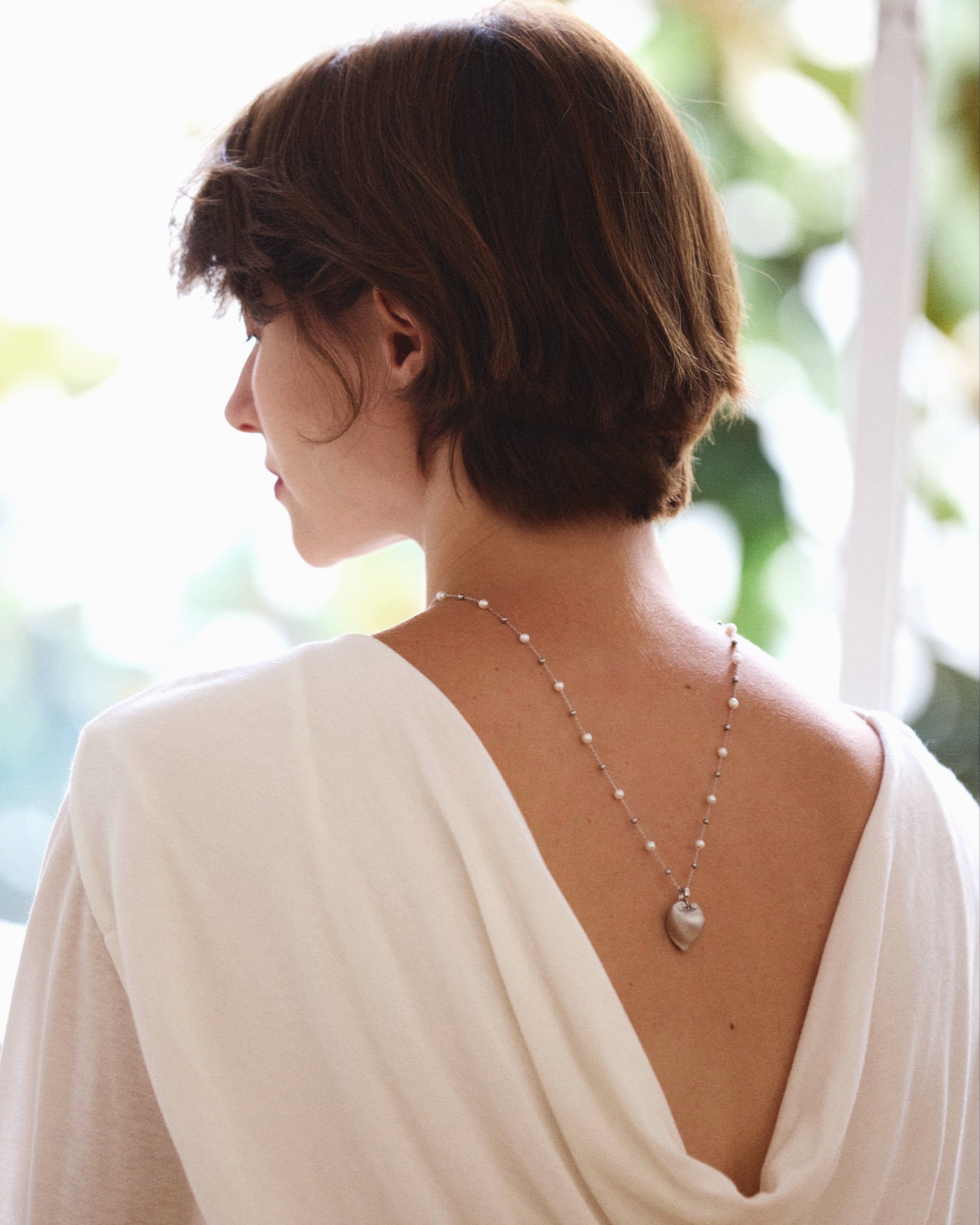 Woman wearing a white open-back dress with a necklace, standing outdoors.