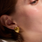 Close-up of a person wearing gold heart-shaped earrings.