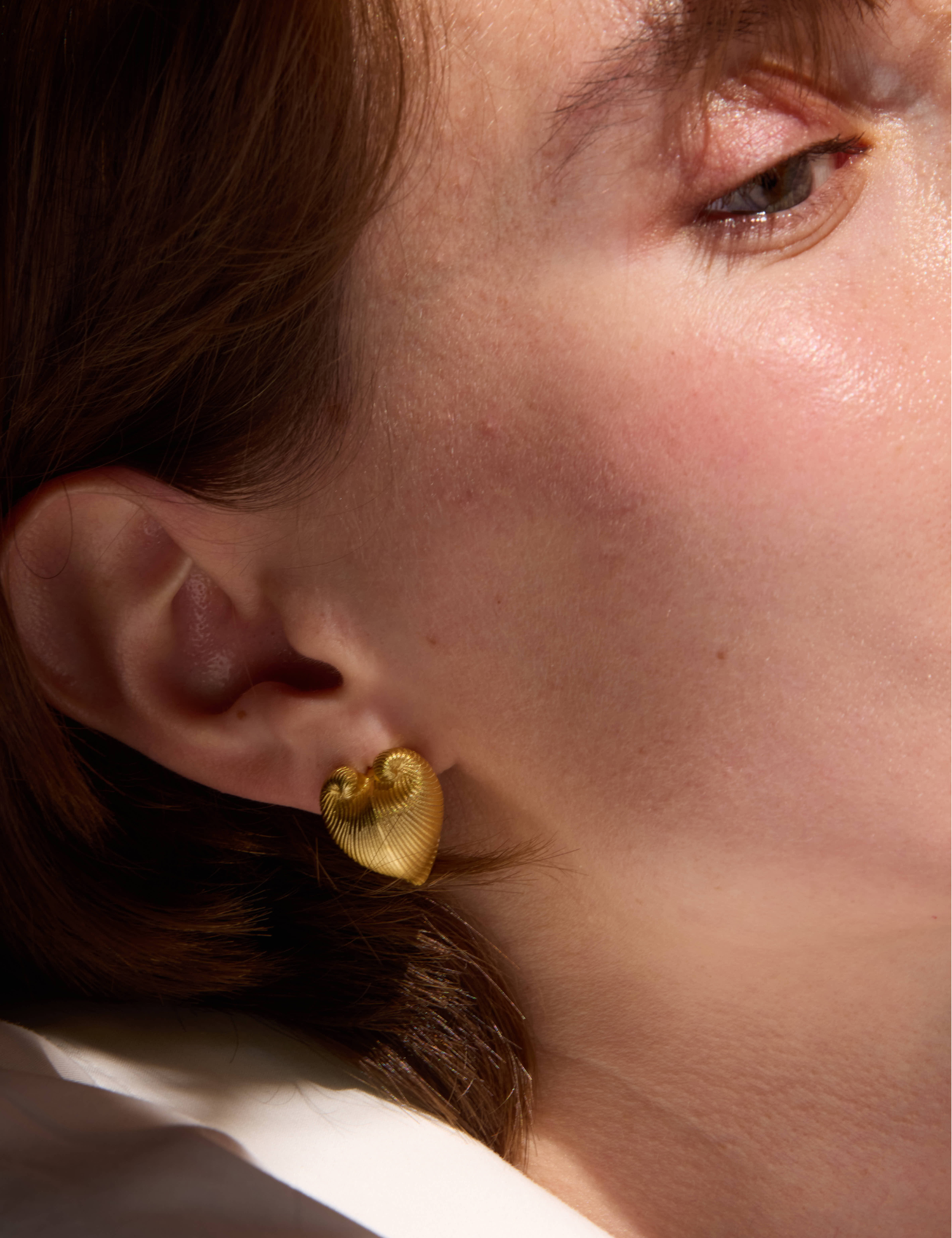 Close-up of a person wearing gold heart-shaped earrings.