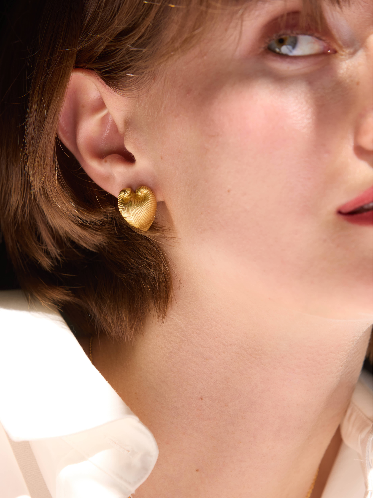 Close-up of a person wearing gold hoop earrings with a blurred background