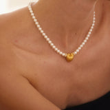 Pearl necklace with gold heart pendants worn by a person