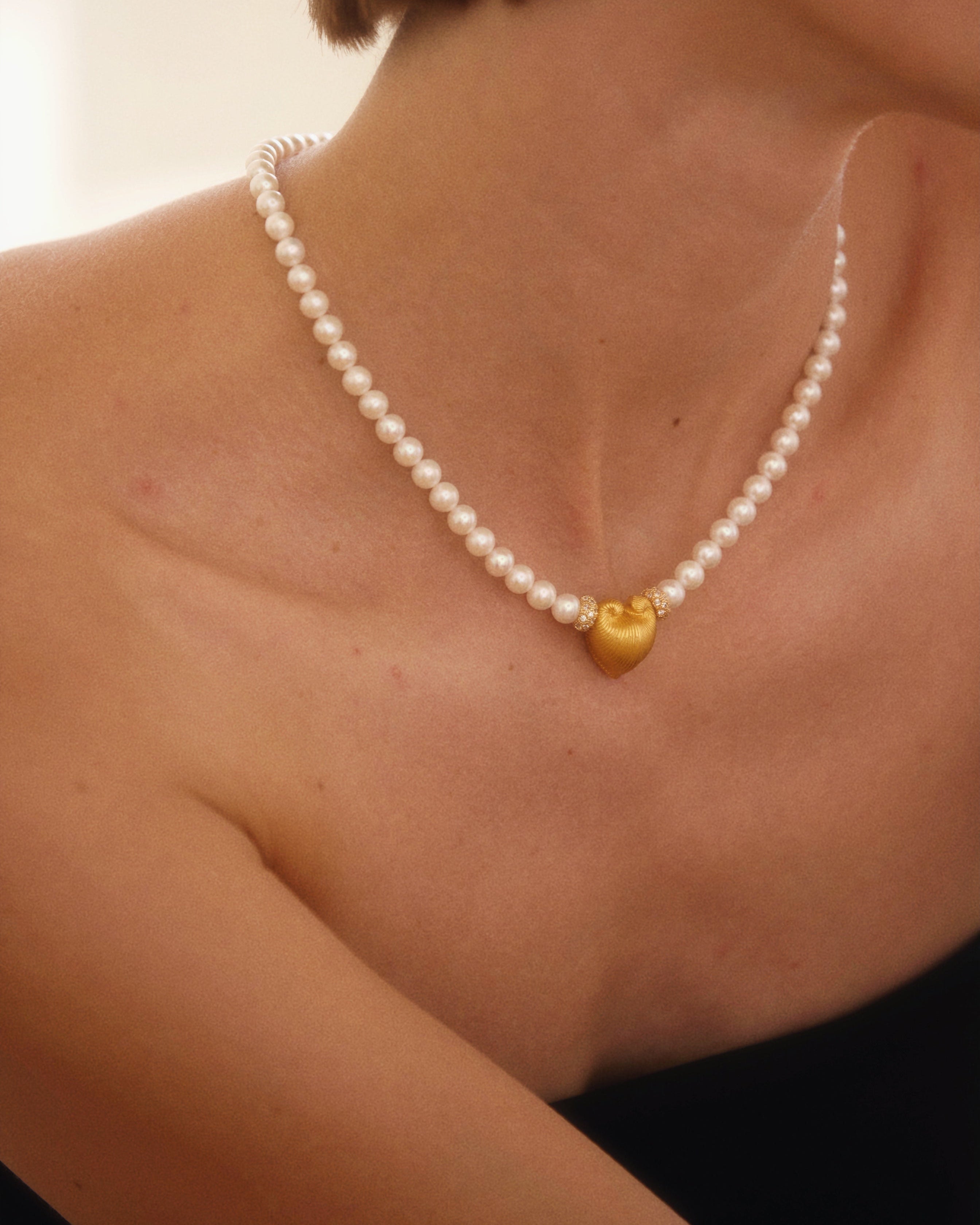 Pearl necklace with gold heart pendants worn by a person