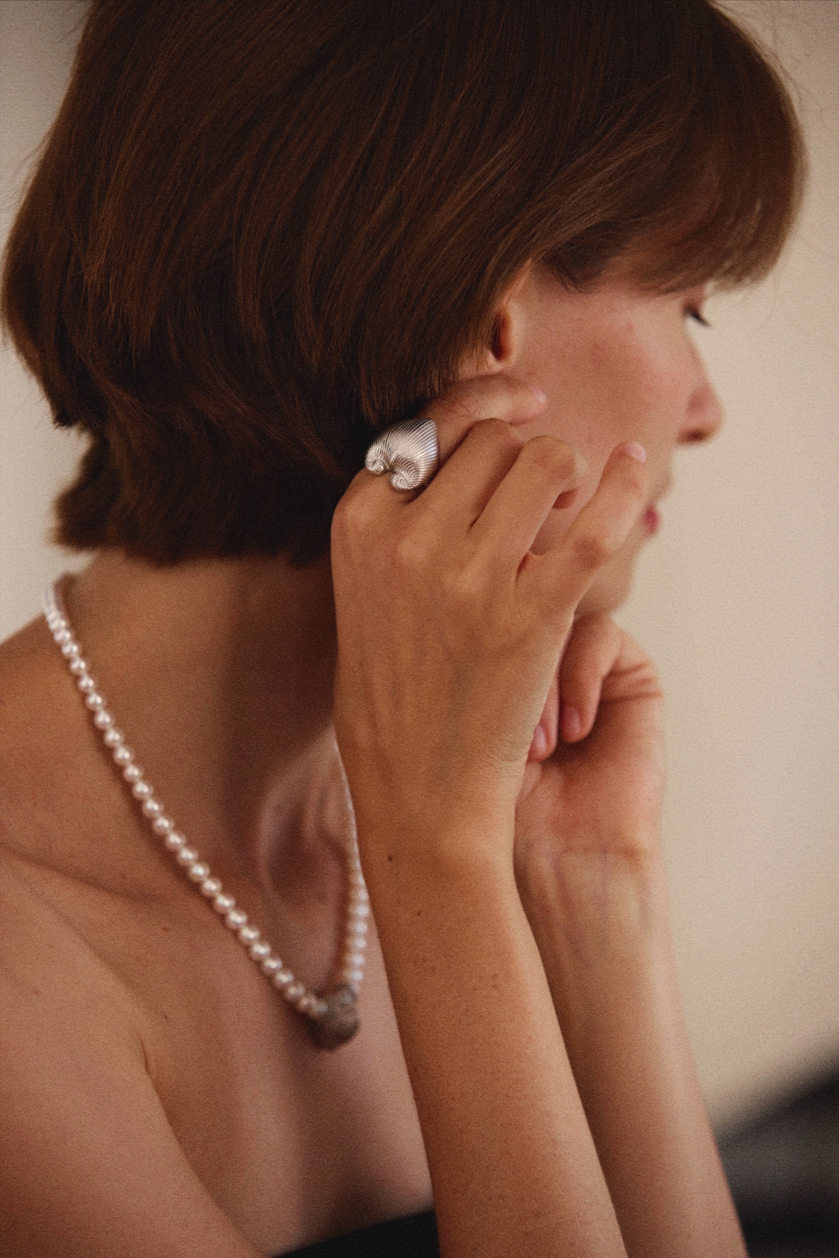 Woman adjusting an earring with a pearl necklace