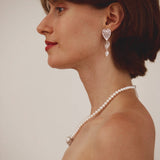 Woman wearing a pearl necklace and earrings against a plain background