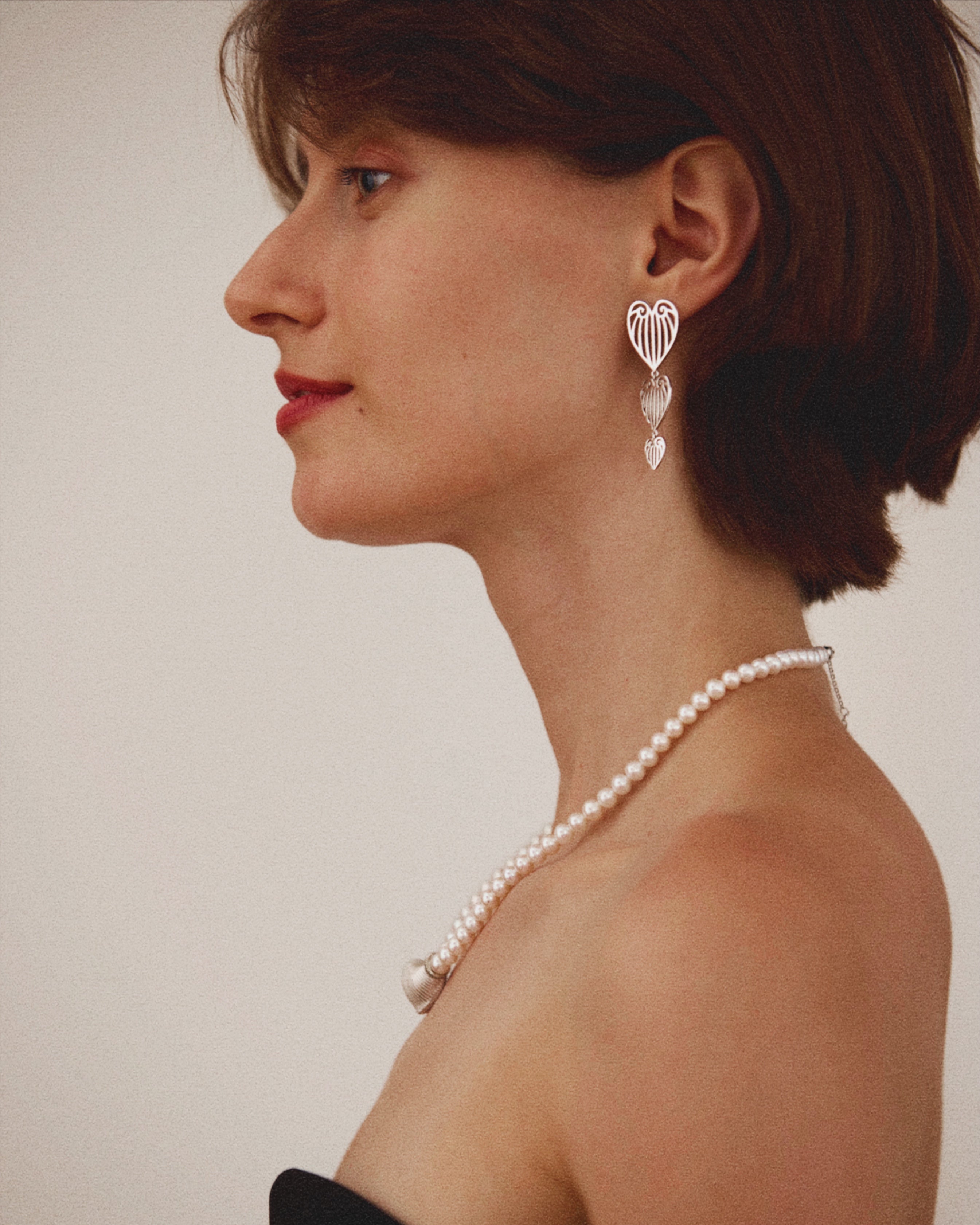 Woman wearing a pearl necklace and earrings against a plain background