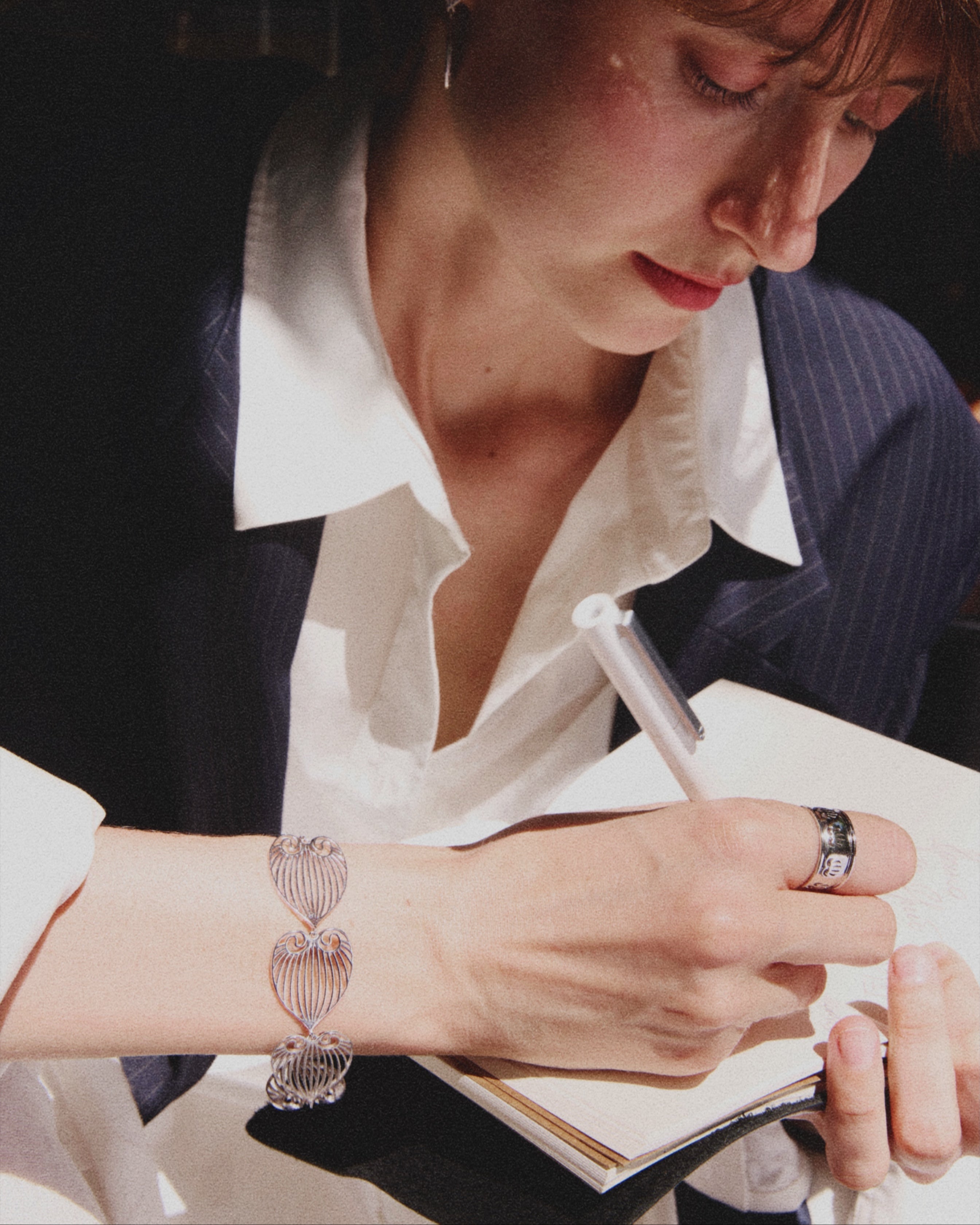 Woman writing in a notebook with a pen, wearing a white shirt and dark blazer.