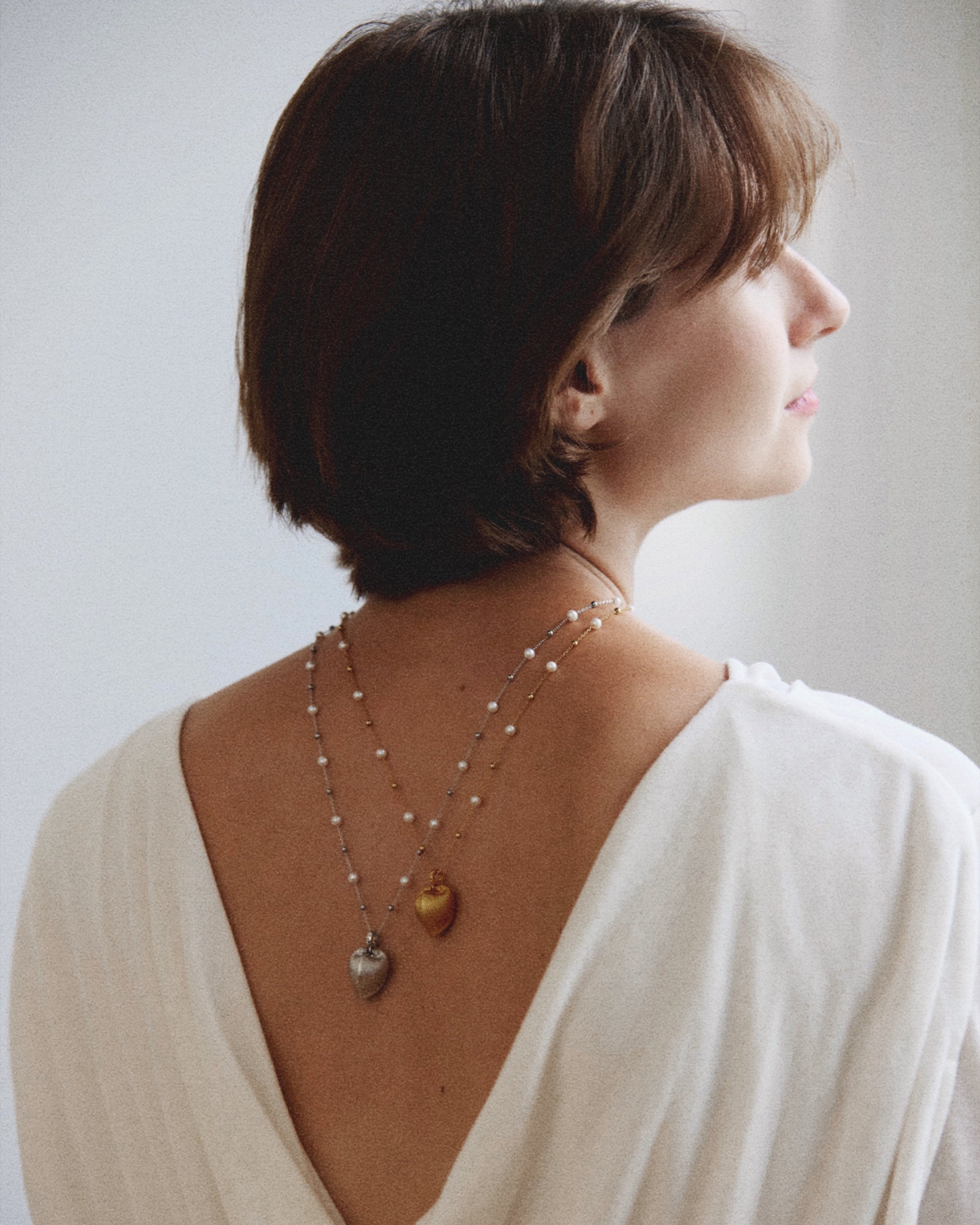 Woman wearing a white garment with a deep neckline, revealing a necklace on her back.