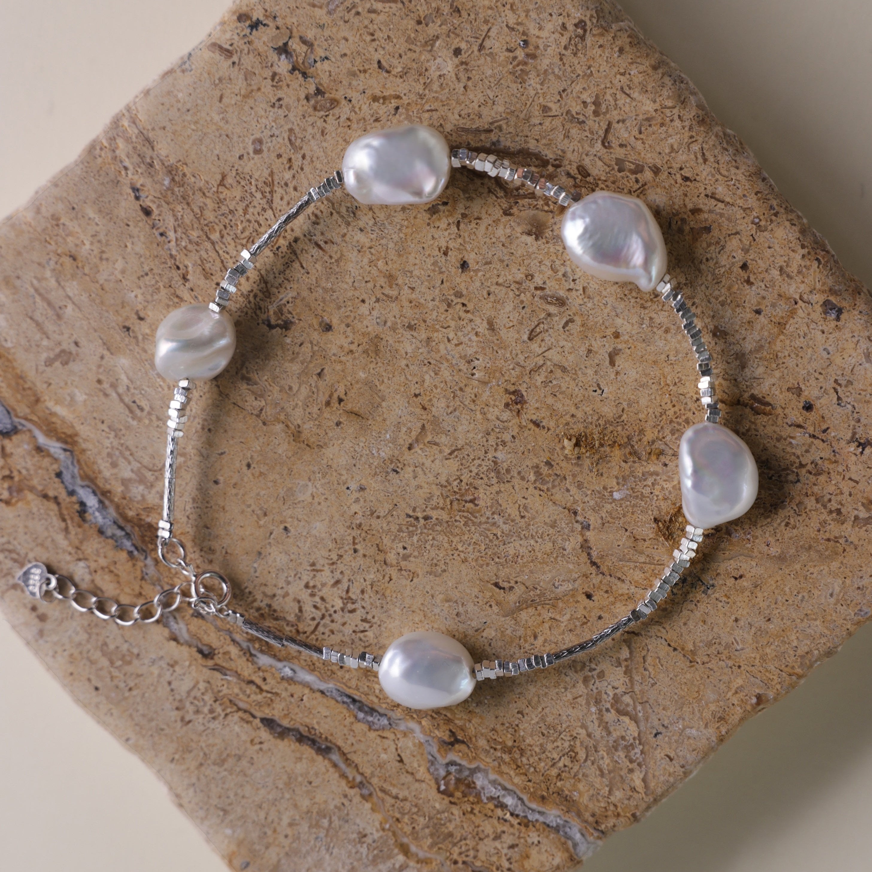 Materials:
- Pearls: Five lustrous Keshi pearls, each about 10mm long.
- Metal: High-quality 925 Sterling Silver for all hardware and detailing.
- Length: The bracelet measures 18.5 cm, featuring an adjustable chain for a customized fit.
Design Highlights: 
This piece is skillfully crafted, showcasing a minimalist yet striking design. The irregularity of the Keshi pearls provides a modern twist on a classic bracelet, complemented by delicate sterling silver accents that add a refined touch.
Styling Tips:
- 