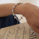 Hand wearing a pearl bracelet holding a book titled 'Pamela'.