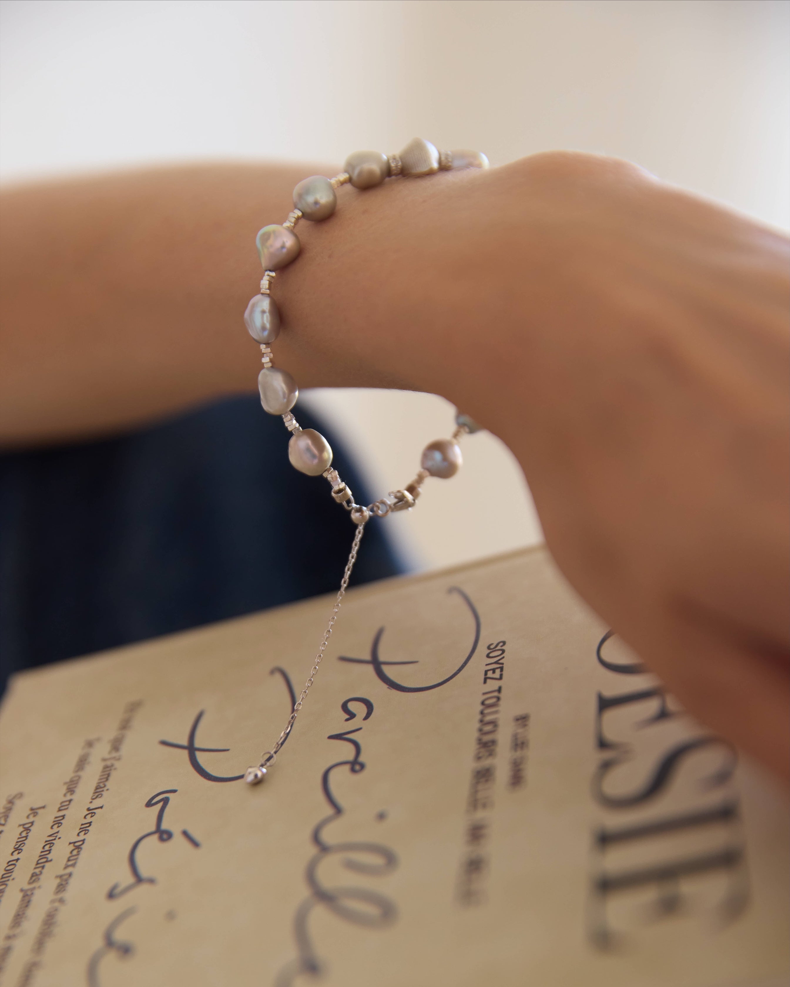 Hand wearing a pearl bracelet holding a book titled 'Pamela'.