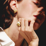 A woman wearing gold heart earrings with a dark background