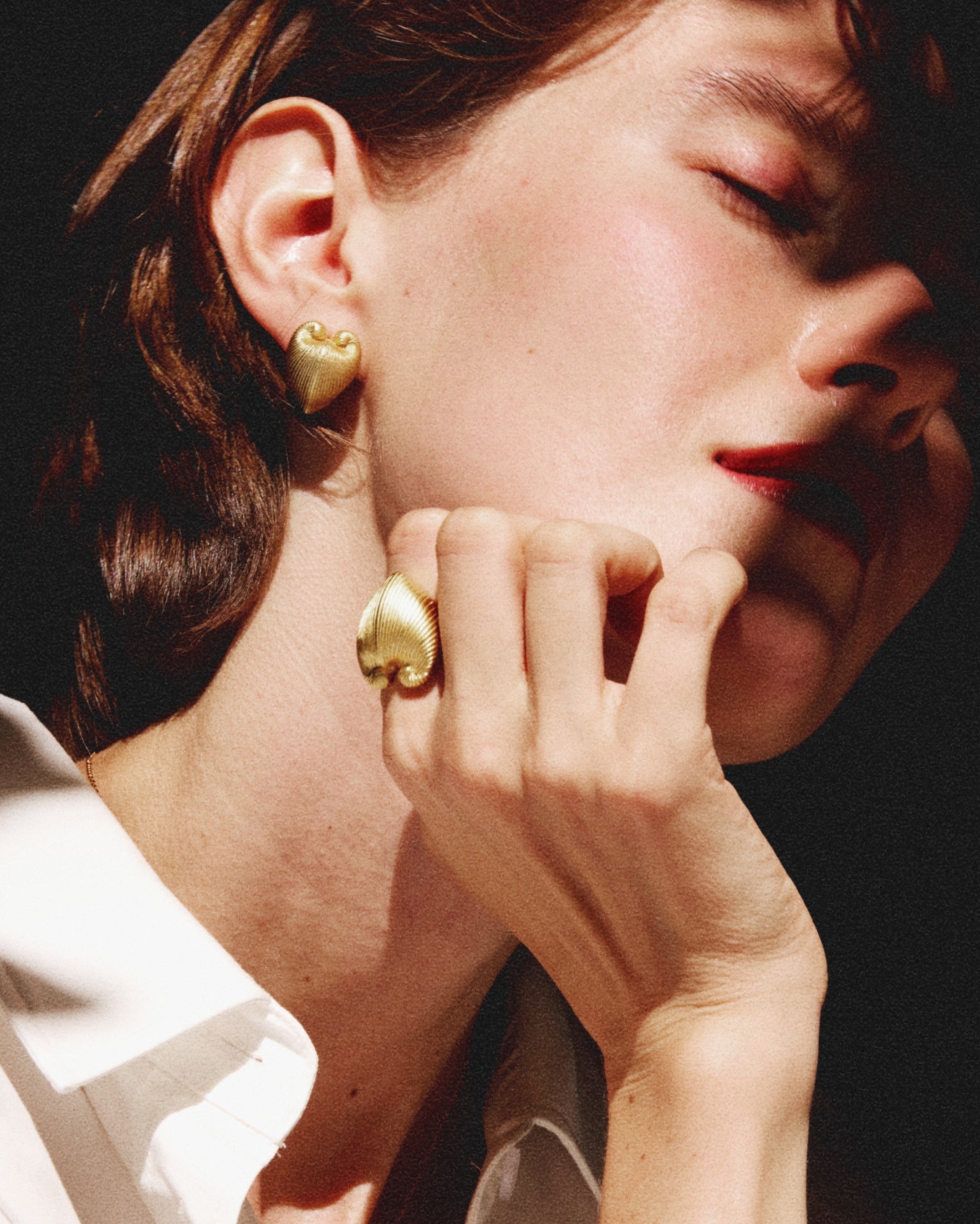 A woman wearing gold heart earrings with a dark background