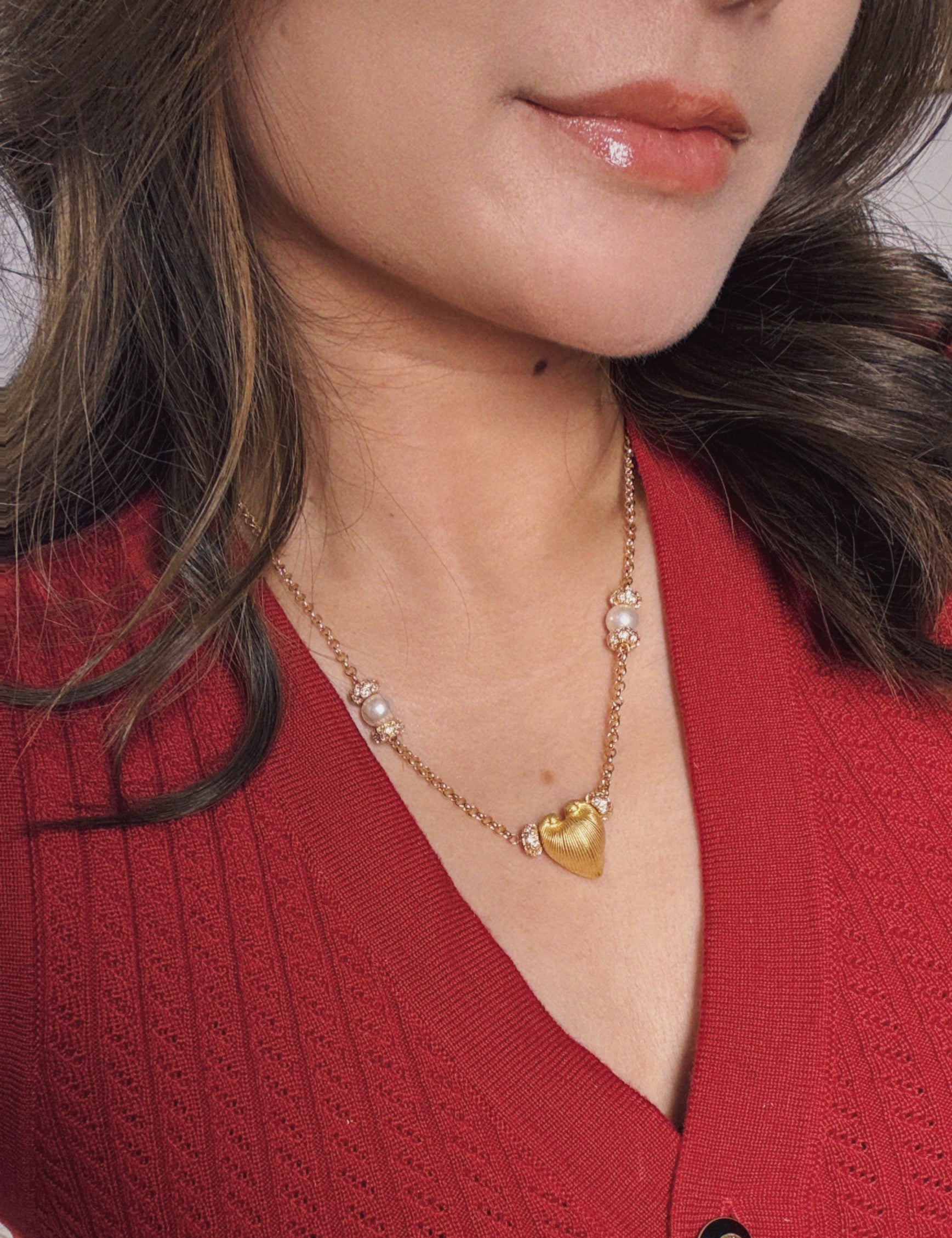 Close-up of a person wearing a gold necklace with a heart-shaped pendant against a red background.