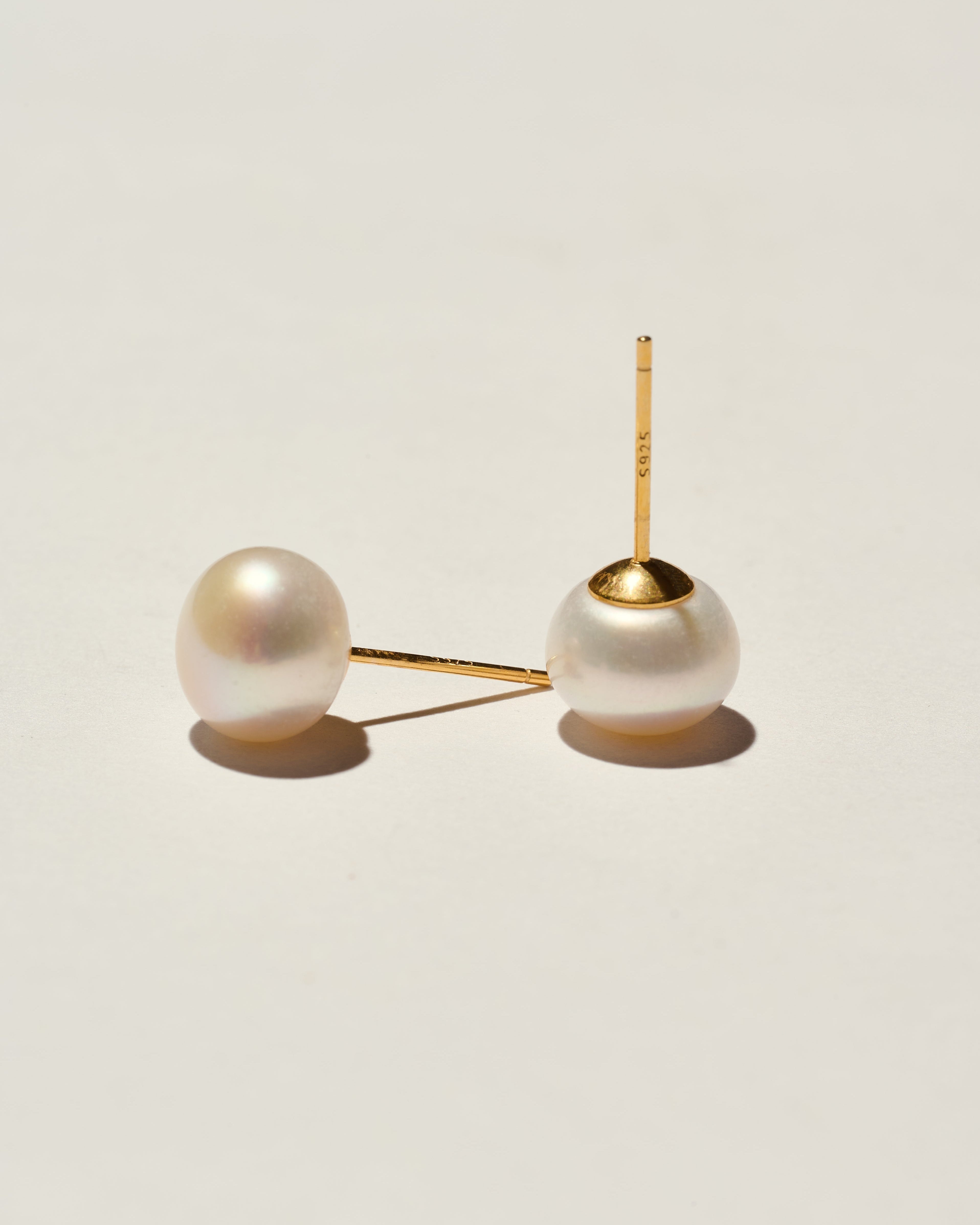 Pair of pearl earrings with gold clasps on a light beige background