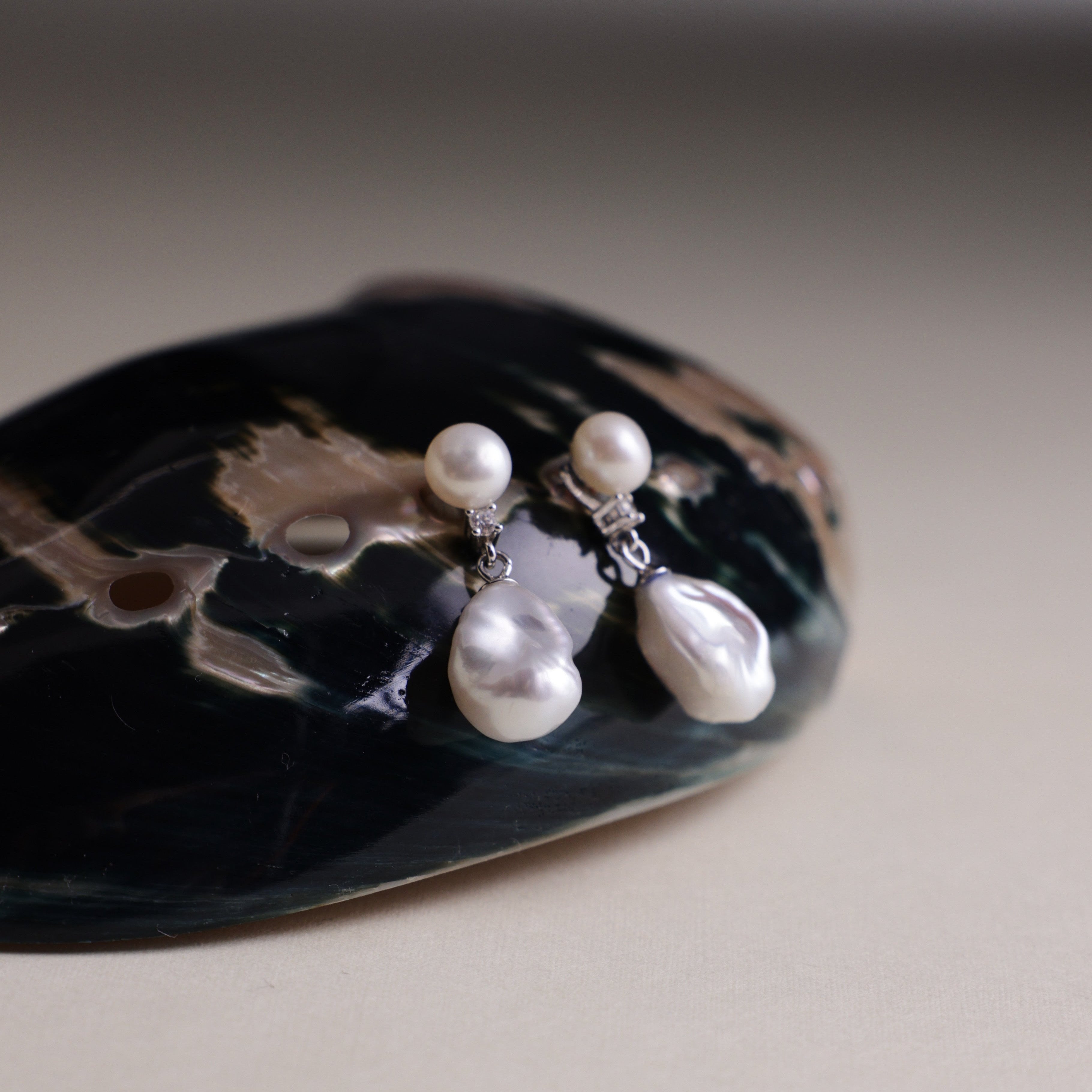 These earrings feature a detachable design that allows you to wear the round pearl with zircon accents for a minimalist look, or add the Keshi pearl for a more dramatic effect. The unique combination of differently shaped pearls with sterling silver and zircon detailing creates a stunning visual contrast, while the versatility of the design makes these earrings a must-have addition to any jewelry collection.
Materials:
- Pearls: One 10mm Keshi pearl and one 6-7mm round pearl on each earring.
- Metal: All co