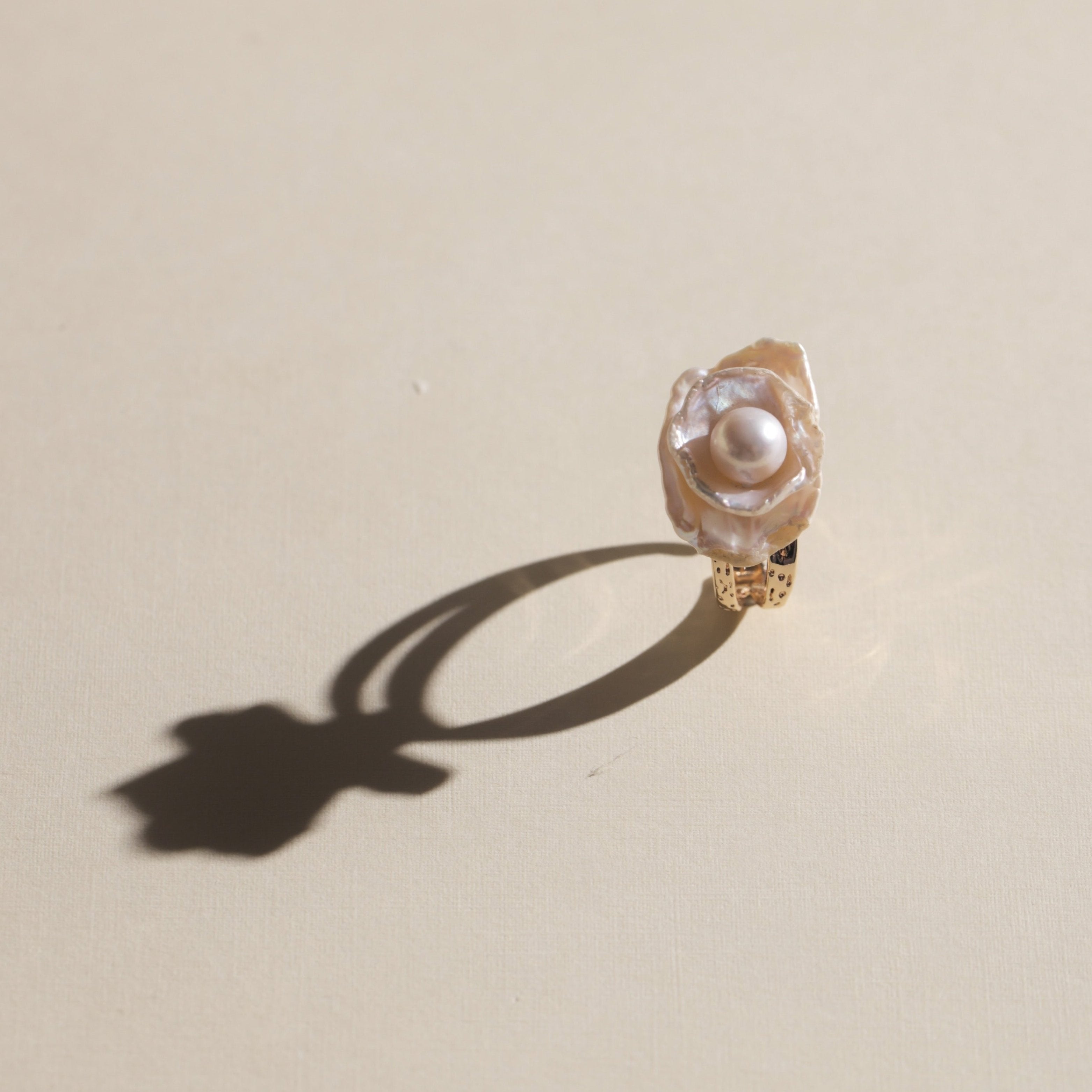 This exquisite floral ring is crafted from rare Keshi petal pearls and topped with a lustrous round freshwater pearl at its center. The natural petal pearls beautifully mimic the delicate petals of a rose, creating a unique and captivating design. The Keshi pearls, known for their irregular shape and stunning luster, make this ring a one-of-a-kind piece that’s perfect for any occasion.Ring is made using high-quality Keshi petal pearls and a freshwater pearl, set on an 18k gold-filled adjustable band