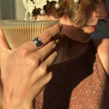 Person holding a glass of coffee with a decorative headpiece and pearl hair accessories.